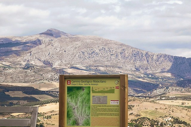 An information board with a map of a stage of the GR 340 walking trail, against a background of rocky mountains